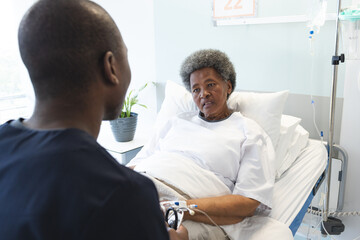 African american male doctor talking with senior female patient in hospital room