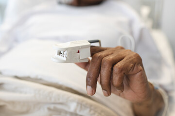 Hand of african american senior female patient lying in bed in sunny hospital room