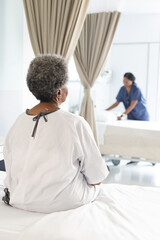 Obraz premium Back of african american senior female patient sitting on bed in sunny hospital room