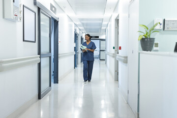 African american female doctor with documents walking in hospital corridor