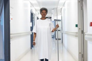 Fototapeta na wymiar African american senior female patient with drip standing in hospital corridor