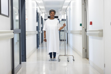 African american senior female patient with drip standing in hospital corridor