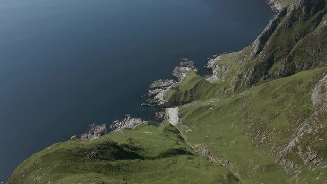 Aerial flyover edge showing green mountains and blue ocean in Norway - Hoddevik Mountain range in summer . Stunning drone top down