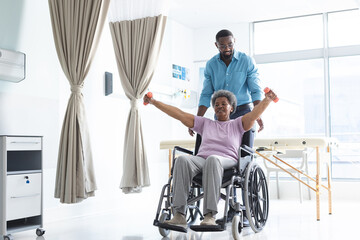 African american senior woman exercising with weights and male doctor advising in hospital room