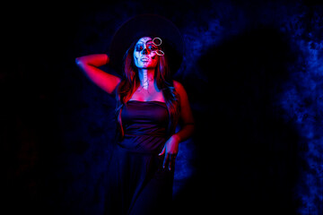 Fototapeta na wymiar A women with Halloween Makeup in blue red light giving out a horror look wearing black gown in black background