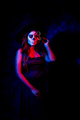 A women with Halloween Makeup in blue red light giving out a horror look wearing black gown in black background