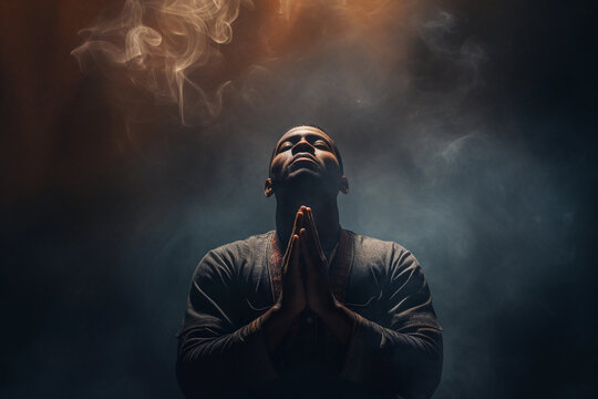 Black man praying in the dark room with his hands folded in prayer
