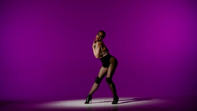 Framed against a purple background. Young woman, showing dance moves towards high heels. A spotlight beam shines on her, the edges of the background are darkened. She is sexy, rhythmic, plastic