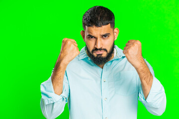Aggressive angry Indian young man trying to fight at camera, shaking fist, boxing with expression, punishment, threaten, bullying, abuse, mad fury. Arabian guy isolated on green chroma key background