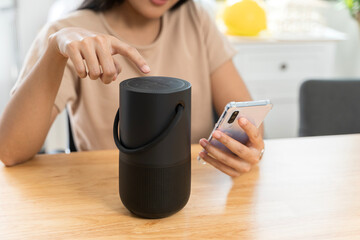 Close-up of a wireless speaker in front of a woman sitting on a work desk at home.
