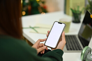Young female freelancer using mobile phone at desk in living room during Christmas time