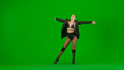 Framed on a green background, chromakey. Young woman wearing open clothing and jacket. Demonstrates a dance movement in the direction of high heels, spreading her arms. She is sexy, plastic.