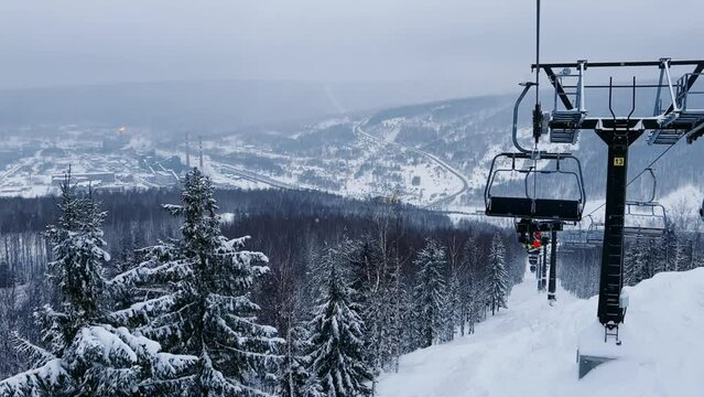 A chairlift at a ski resort on a cloudy winter day in the Ural Mountains. A lift on the background of factory pipes. Climbing the mountain. Gubakha, Perm Krai, 4K