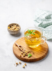 Chamomile herbal tea in a glass cup with mint on a light background with dry flowers. The concept of a healthy detox drink for health and sleep.