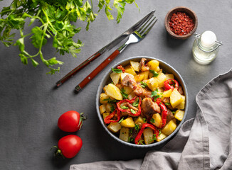 Fried pork meat with potatoes, onions and peppers. National homemade Georgian dish ojakhuri in a bowl on a dark background with spices, fresh tomato and herb.