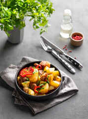 Fried pork meat with potatoes, onions and peppers. National homemade Georgian dish ojakhuri in a black frying pan on a dark background with spices and fresh herb.