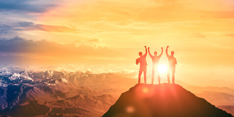 Silhouettes of businessmen working as team on top of mountain on backdrop of bright colorful...