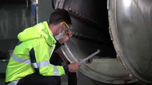technician engineer worker wear mask holding clipboard sitting to checking boiler tank in factory
