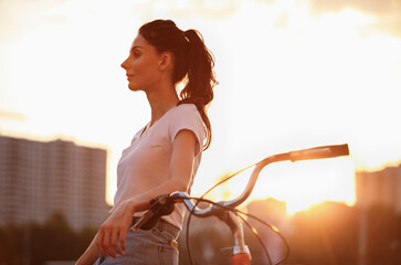Beautiful young woman chilling with a bike in the city street at sunset