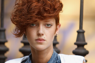 Portrait of a stylish young woman with curly red hair and lip piercing