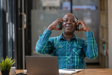 Senior black man wearing headphones enjoying listening to music or something interesting to relax while working.
