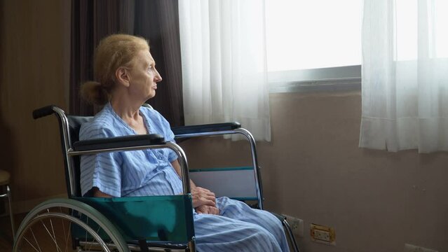 senior woman patient sit on wheelchair alone and looking out the window at hospital ward . Lonely old female in Nursing home. loneliness elder. Depressed mature