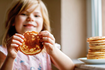 Little happy preschool girl with a large stack of pancakes for breakfast. Positive child eating...
