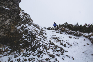 A lonely hiker tourist woman descends down a snow covered ice and a steep cliff on the background...