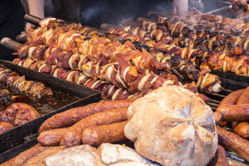 A lot of different meats and sausages are on the counter and grilled,  during the street festival