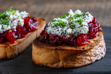 Toast from a slice of bread with white cream cheese, stewed beetroot pulp, seeds and green dill on wooden board. Delicious breakfast on morning. Closeup