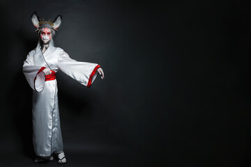 Pretty actress woman with stage makeup, rabbit mask and costume standing on black background....