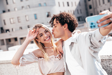 Young smiling beautiful woman and her handsome boyfriend in casual summer clothes. Happy cheerful family. Female having fun. Couple posing in the street background at sunny day. Take selfie photos