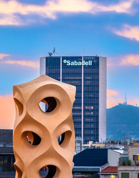 Barcelona, Spain - October 7, 2023: Headquarters of the bank Sabadell in Barcelona, Catalonia, Spain. A sculpture on the roof of the house Pedrera in foreground