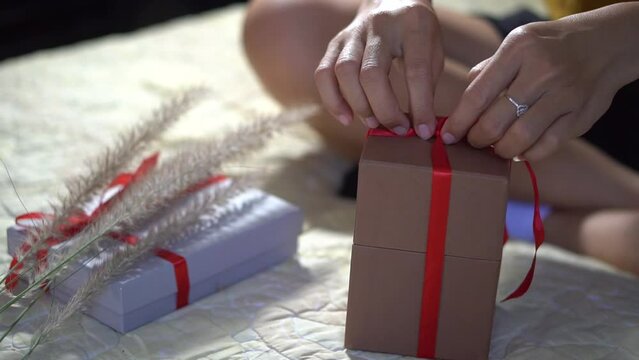 Female hands wrapping Christmas gift in tying red ribbon