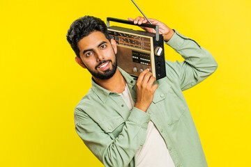 Happy young Indian man using retro tape record player to listen music, disco dancing favorite track, having fun entertaining, fan of vintage technologies. Arabian guy isolated on yellow background