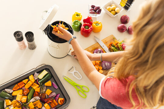 Happy blonde caucasian woman composting vegetable waste in sunny kitchen at home