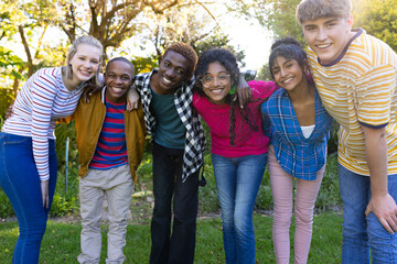 Portrait of happy diverse teenage friends embracing in sunny park