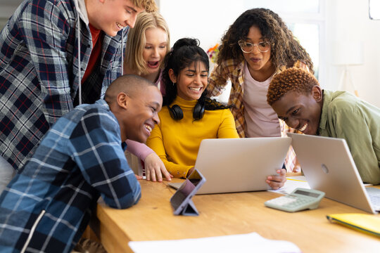 Happy diverse group of teenage friends studying with laptop and tablets at table at home