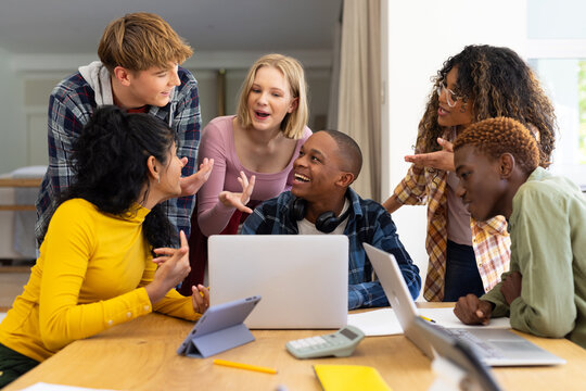 Happy diverse group of teenage friends studying with laptop and tablets at table at home