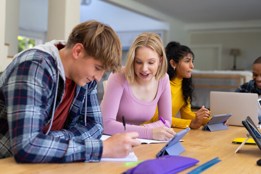 Happy diverse group of teenage friends studying with laptop and tablets at table at home