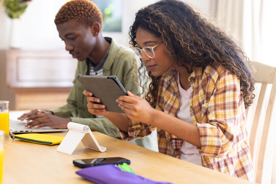 Happy diverse teenage friends studying with tablet and laptop at table at home - Powered by Adobe