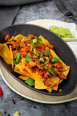 nachos with sauce, meat and herbs in a black plate, side view