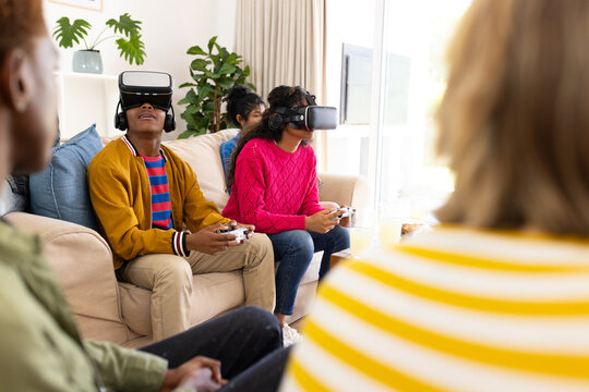 Happy diverse group of teenage friends using vr headsets and playing video games at home