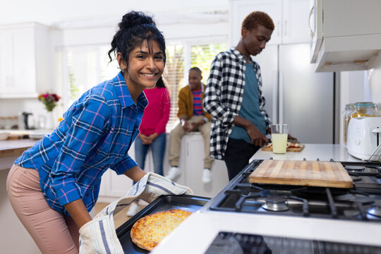 Portrait of happy diverse group of teenage friends cooking and making pizza in kitchen - Powered by Adobe
