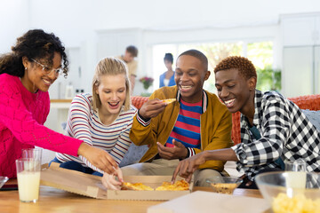 Happy diverse group of teenage friends with snacks and drinks eating pizza on couch