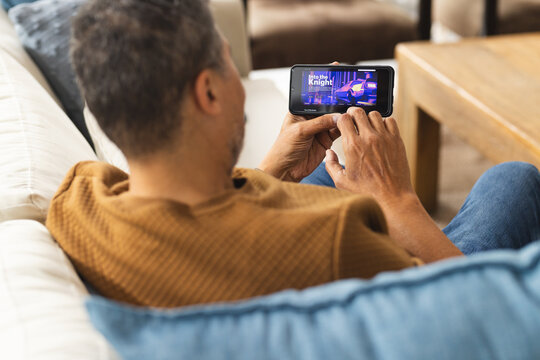 Happy Senior Biracial Man Sitting On Couch And Watching Movie On Smartphone At Home