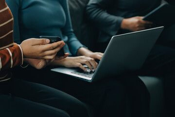 Three beautiful Asian girls using smartphone and laptop, chatting on sofa together at cafe with copy space, modern lifestyle with gadget technology or working woman on casual business concept