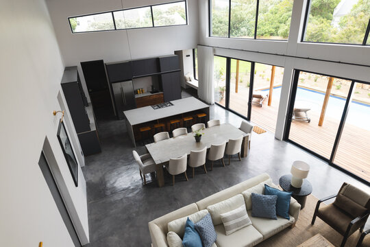 Big empty modern kitchen and living room with wooden table, big white couch and big windows