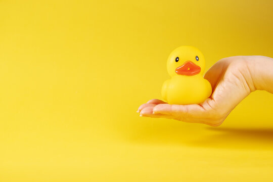 rubber duck in hand on yellow background, baby's bath accessory, creative playtime, yellow ducky
