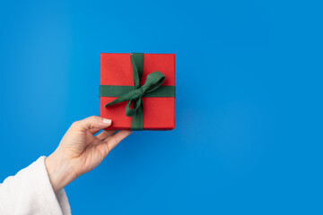 Hand with a gift box on a blue background, New Year's present, ribbon wrap, festive decoration